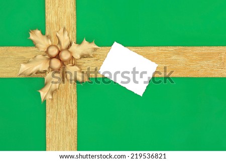 Christmas gift box background in green with gold bauble decorations, ribbon, holly and white tag.