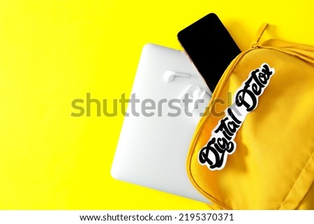 Different gadgets in bag with words DIGITAL DETOX on yellow background, flat lay. Space for text