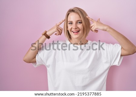 Young caucasian woman standing over pink background smiling pointing to head with both hands finger, great idea or thought, good memory 