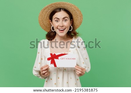 Young happy smiling woman she 20s wears white dress hat hold gift certificate coupon voucher card for store isolated on plain pastel light green background studio portrait. People lifestyle concept