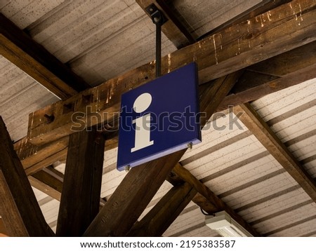 Information symbol at a train station building. Letter i on a blue metal plate hanging on the rooftop of a building. Info point for tourists and passengers. Public transportation in an urban area.