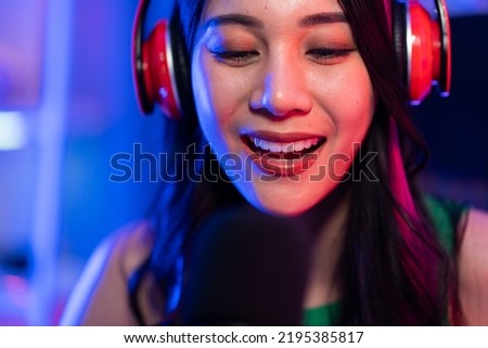 Asian attractive audio DJ woman speaks into microphone to broadcasting. Young beautiful female blogger influencer wearing headphones and recording morning news podcast show for radio at home studio.