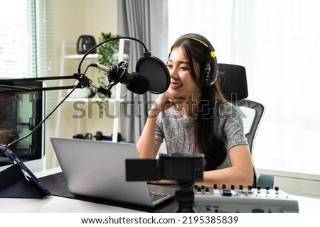 Asian attractive audio DJ woman speaks into microphone to broadcasting. Young beautiful female blogger influencer wearing headphones and recording morning news podcast show for radio at home studio.
