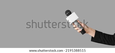 Journalist's hand holding microphone on grey background with space for text Royalty-Free Stock Photo #2195388515