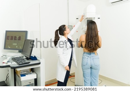 Female technician wearing a lab coat doing a breast mammogram exam on a young woman at the medical diagnostic center