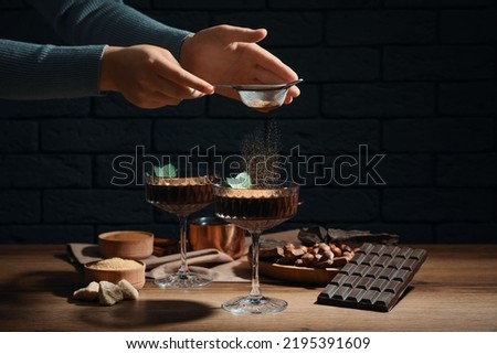 Woman decorating hot chocolate with cocoa powder at wooden table, closeup