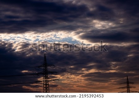 Golden sky with sun rays and lens flare shows solar energy with electricity tower pylon silhouette in golden sunset and orange sky for sustainable energy or renewable resources from dusk till dawn sun