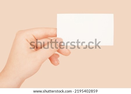 Female hands holding white blank paper sheet mockup on beige background.                                 