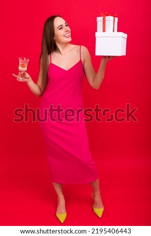 Christmas holidays. A young woman in a stylish dress with champagne and gift boxes on a red background