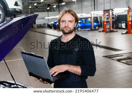 Portrait of a professional automotive electrician who diagnoses car errors using a laptop against the background of a service station