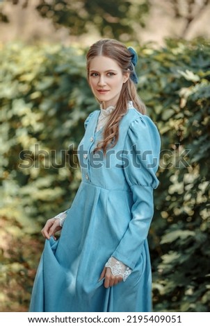 Young beautiful girl dressed in a blue vintage dress with a bow on her head. Victorian girl in a blue dress walking in the park. Young noblewoman on a walk.	 Royalty-Free Stock Photo #2195409051