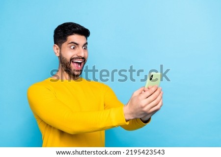 Photo of pretty impressed guy dressed yellow pullover chatting modern gadget empty space isolated blue color background