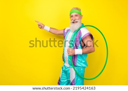 Portrait of handsome positive aged person hold hula-hoop direct finger empty space isolated on yellow color background