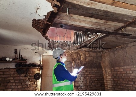 Building inspector. Man in a hard hat and a yellow reflective vest examines damaged structures and inspects the building. Damage assessment. Preparing for the repair or construction of a building Royalty-Free Stock Photo #2195429801