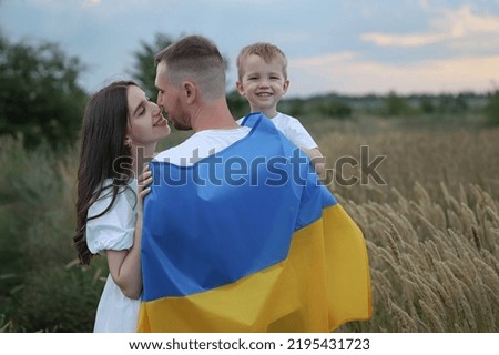 dad stands with his back with a flag and hugs his wife and son. High quality photo