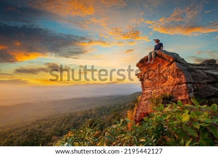 man sitting on a cliff,Young man with backpack sitting on rock looking into the landscape. Listening to the silence. Beautiful moment the miracle of nature. Royalty-Free Stock Photo #2195442127