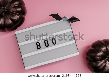 Flat lay with Lightbox with text Boo , black pumpkins and bat silhouettes on the pink backgound.