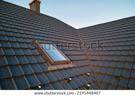 Closeup of attic window on house roof top covered with ceramic shingles. Tiled covering of building Royalty-Free Stock Photo #2195448407