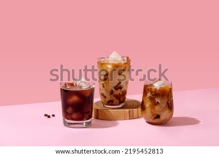 Ice coffee in a tall glass with cream poured over and coffee beans. Set with different types of coffee drinks on a pink table. Royalty-Free Stock Photo #2195452813
