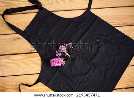the florist's black apron lies on a wooden table in a pocket of pink flowers. Space for the text.