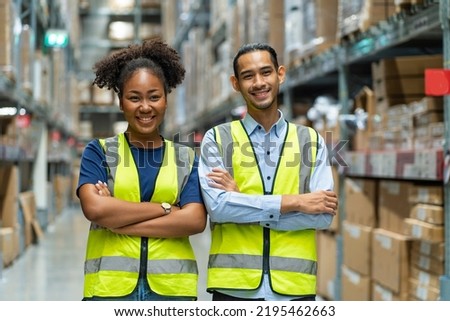 Asian male and African American female employees wearing colleague uniforms standing with their arms crossed and proud of warehouse and freight service. Royalty-Free Stock Photo #2195462663