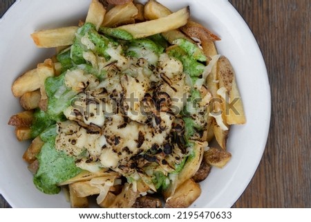 French fries. Top view of a bowl with fried potatoes with spinach cream, mozzarella, cheddar, danvo and blue cheese, in a white bowl on the wooden table.