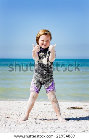 young girl covered in sand giving the thumbs up sign