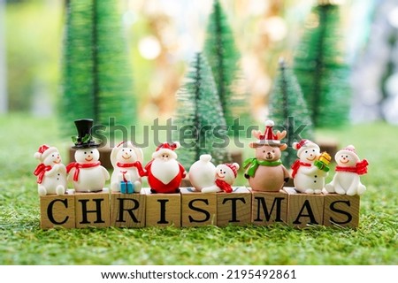 CHRISTMAS letter on wooden block with tiny toy Santa, reindeer, snowman and blurred christmas trees background