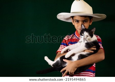 A boy with pet cat in hands wearing white hat on green background 