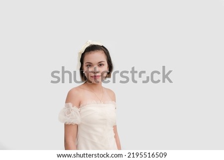 A petite young woman wearing a white lace dress and a ribbon on her hair standing naturally isolated on a white background.