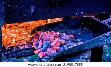 Using a shovel to bring the coals to the flame inside the grill. Shovel for hot coals. Burning coal on a shovel