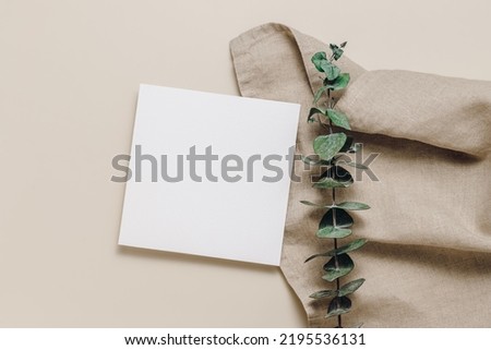 Blank paper card on linen cloth and eucalyptus leaves. Top view, flat lay. Minimal aesthetic card with copy space