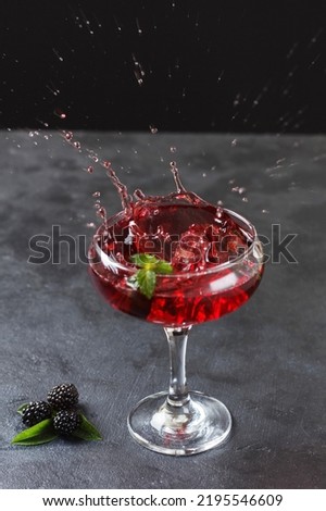 Splash of blackberry cocktail in a glass on a black background.