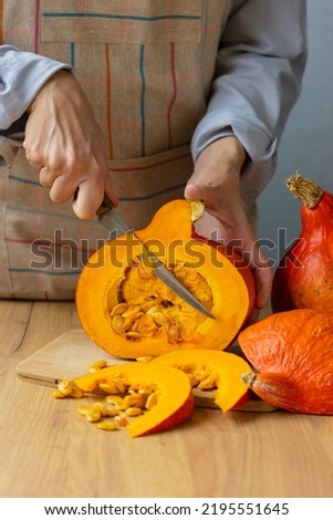 woman cuts orange pumpkins with a knife on a cutting board in the kitchen. cooking pumpkin is an eco-friendly food for the whole family. Halloween and All Saints' Day celebrations, autumn holidays