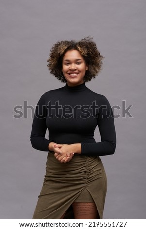 Young cheerful female fashion model in smart casualwear holding her hands in front of herself while looking at you in isolation