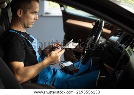 Automotive mechanic running diagnostics software on tablet computer. Mechanic sitting in car and working on laptop while doing vehicle diagnostic test in auto service garage. Royalty-Free Stock Photo #2195556133