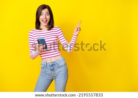 Photo of charming young girl excited sales point empty space hold gadget wear stylish striped outfit isolated on yellow color background