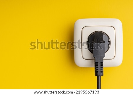 Electric plug and wall socket on an yellow wall. Royalty-Free Stock Photo #2195567193