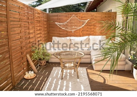 Real photo of relaxing boho zone in home. Wooden floor on terrace with comfy furniture and green plants. Decoration concept. Sunny summer day.
