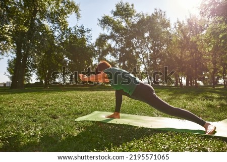 Middle aged woman practicing yoga in park. Sportive female pensioner wearing sportswear standing on fitness mat on green lawn. Concept of healthy lifestyle. Sunny summer daytime