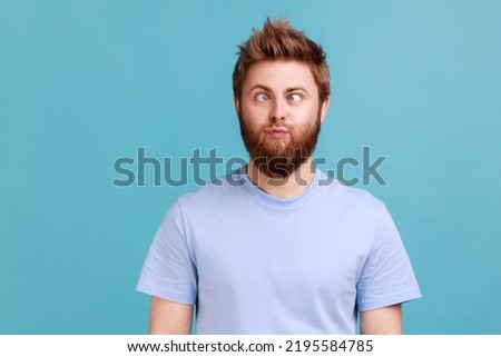 Portrait of man making silly humorous face with eyes crossed, showing comical silly brainless facial expression posing with stupid smile, fooling around. Indoor studio shot isolated on blue background
