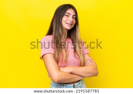 Young caucasian woman isolated on yellow background with arms crossed and looking forward