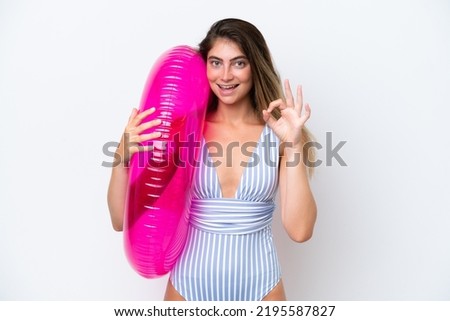 Young woman in swimsuit holding an air mattress donut isolated on white background showing ok sign with fingers