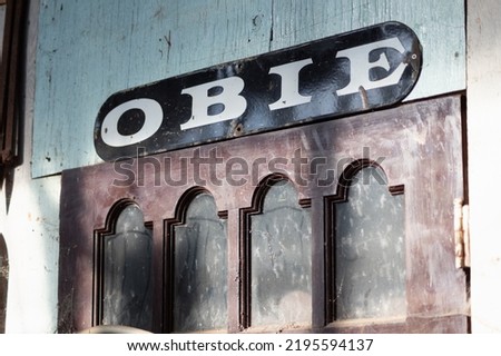 This is an image of a dusty red door with a black sign with white letters that spells, "OBIE" above it.