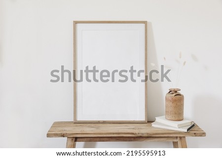 Dry bunny tail, lagurus grass bouquet. Ceramic vase on books. Old wooden bench, table. Blank vertical picture frame mockup. White wall background. Empty copy space. Scandinavian nterior. Autumn still