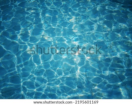 Defocus blurred transparent blue colored clear calm water surface texture with splash, bubble. Shining blue water ripple background. Surface of water in swimming pool. Tropical blue water textures.