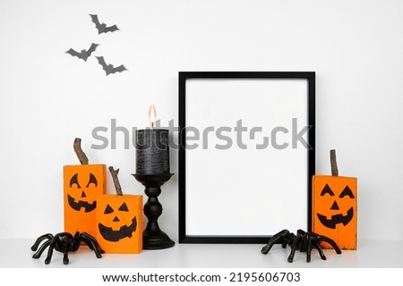 Halloween mock up. Black frame on a wood shelf with rustic wood jack o lantern decor, spiders and candle. Portrait frame against a white wall with bats. Copy space.