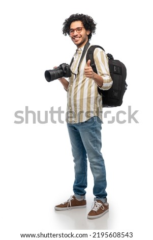 photography, profession and people and concept - happy smiling man or photographer in glasses with digital camera and backpack showing thumbs up gesture over white background