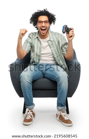 technology, people and leisure concept - happy smiling young man in glasses with gamepad playing video game and celebrating success over white background