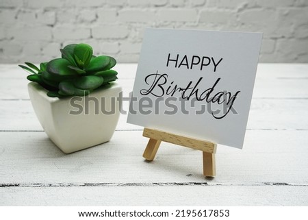 Happy Birthday text on wooden easel standing on white brick wall and wooden background
